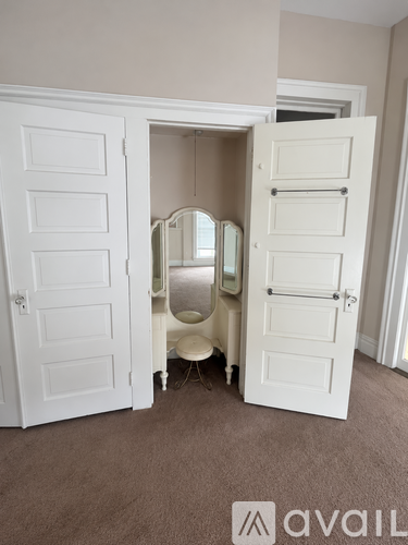 A white wardrobe with a mirror and a white chair is open in a room.