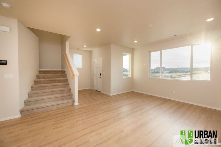 A spacious, empty room with wooden floors and a staircase leading to the upper level.
