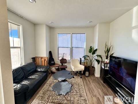 A living room with a black leather couch, a white chair, a wooden coffee table, and a flat screen TV.
