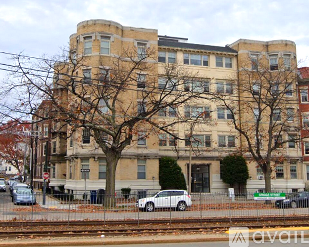 A large beige building with a curved corner and a tree in front of it.