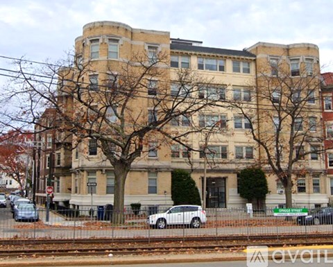 A large beige building with a curved corner and a tree in front of it.