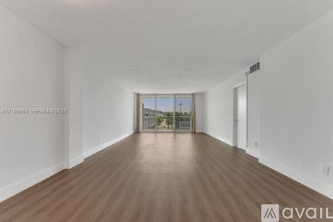 A spacious room with wooden flooring and white walls.