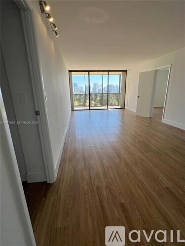 A spacious room with wooden flooring and a view of the city through the sliding glass doors.
