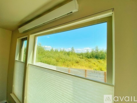 A window with blinds overlooking a grassy area.
