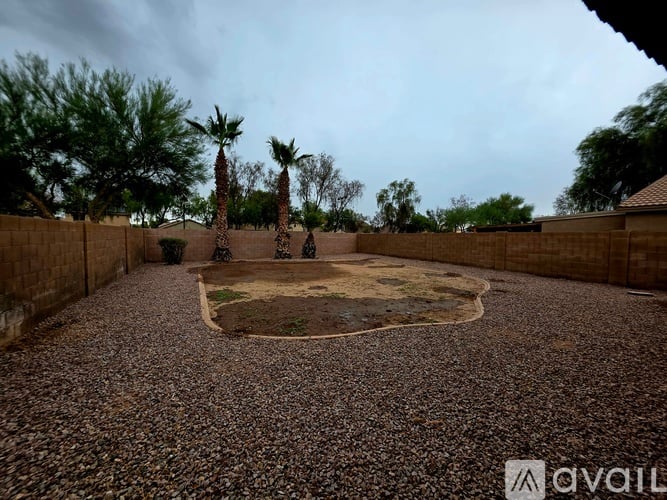 A backyard with a gravel ground and a small patch of grass in the middle.