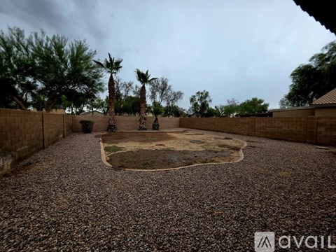 A backyard with a gravel ground and a small patch of grass in the middle.