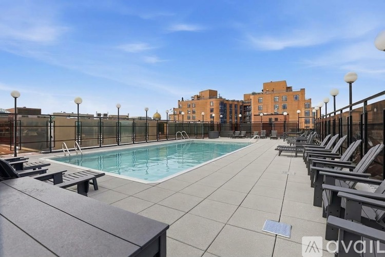 A pool area with lounge chairs and apartment buildings in the background.