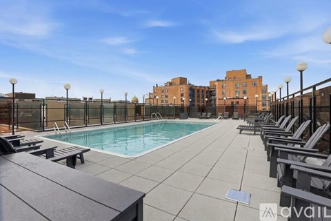A pool area with lounge chairs and apartment buildings in the background.