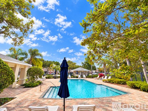 A pool surrounded by trees and chairs with a blue umbrella.