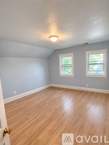 A room with wooden flooring and two windows.