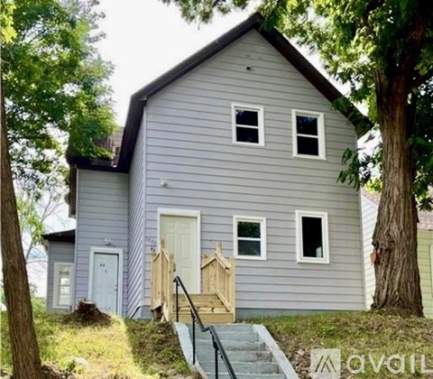 A house with a grey siding and a white door is surrounded by trees.