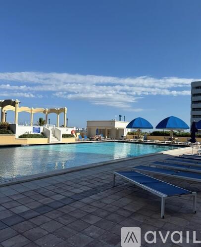 A pool area with sun loungers and a building in the background.