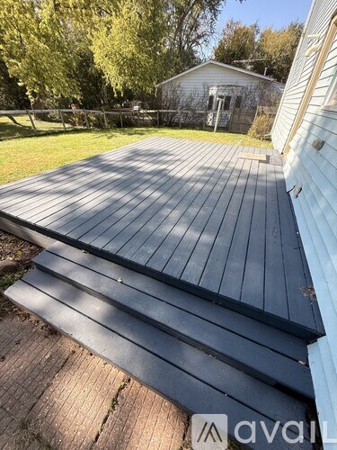 A wooden deck with a house and trees in the background.