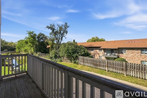 A wooden deck overlooks a grassy area with a house and trees in the distance.