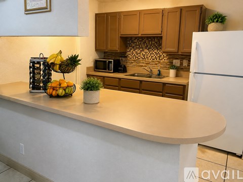A kitchen with a white refrigerator, brown cabinets, and a counter with a bowl of fruit on it.