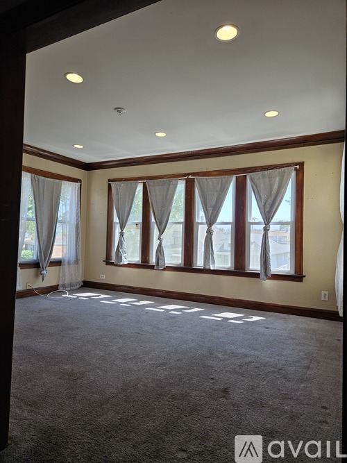 A room with carpeted floor and a large window with curtains.