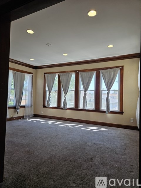 A room with carpeted floor and a large window with curtains.