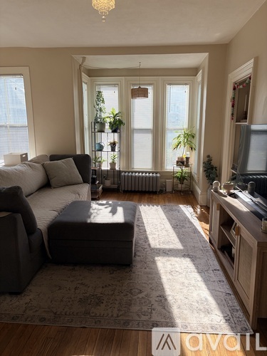 A living room with a grey couch, a black ottoman, and a wooden cabinet.
