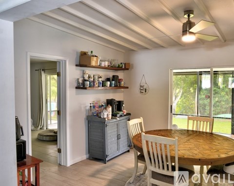 A kitchen with a wooden table and chairs, a cabinet, and shelves with various items.