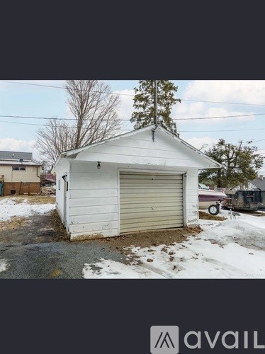 A small white building with a closed grey door is situated in a yard.