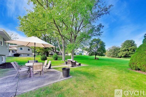 A patio with a table and chairs is surrounded by a grassy area and trees.