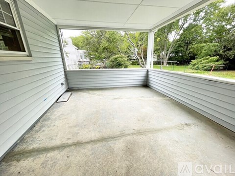A patio area with a concrete floor and a view of trees and a house in the background.