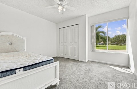 A bedroom with a bed, a ceiling fan, and a window overlooking a green area.