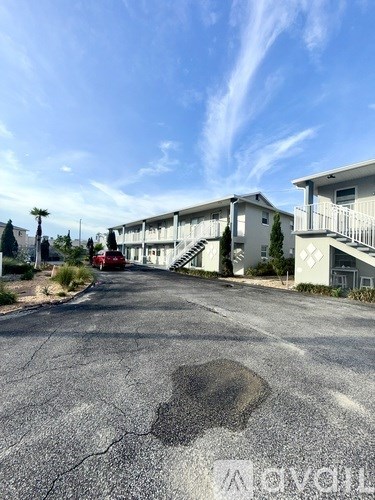 A paved road leads to a white building with a red car parked in front.