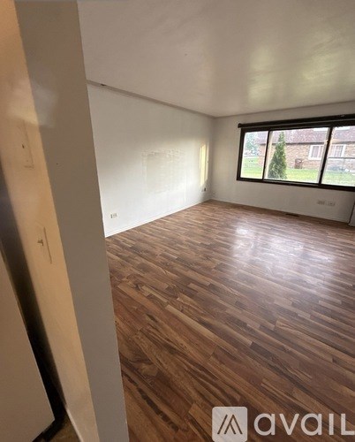 A room with wooden flooring and a window overlooking a building.