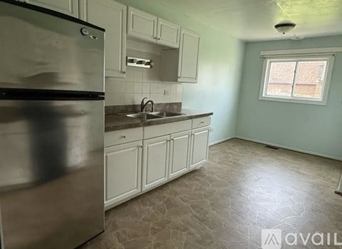 A kitchen with a stainless steel refrigerator, white cabinets, and a stone floor.