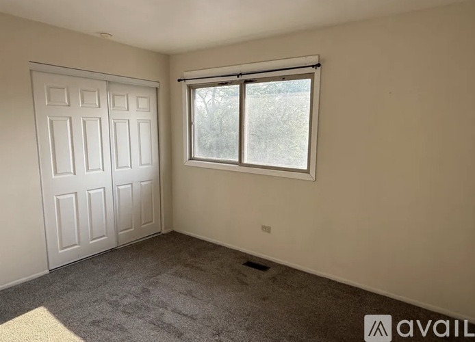 A room with a white door and a window with a view of trees outside.