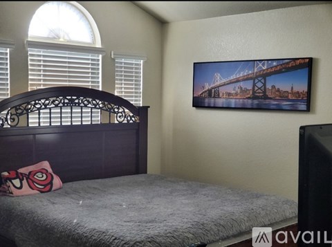 A bedroom with a bed, a window with blinds, and a framed picture of a bridge on the wall.