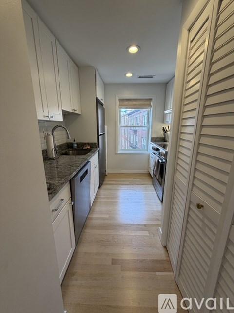 A kitchen with white cabinets and a window overlooking a street.