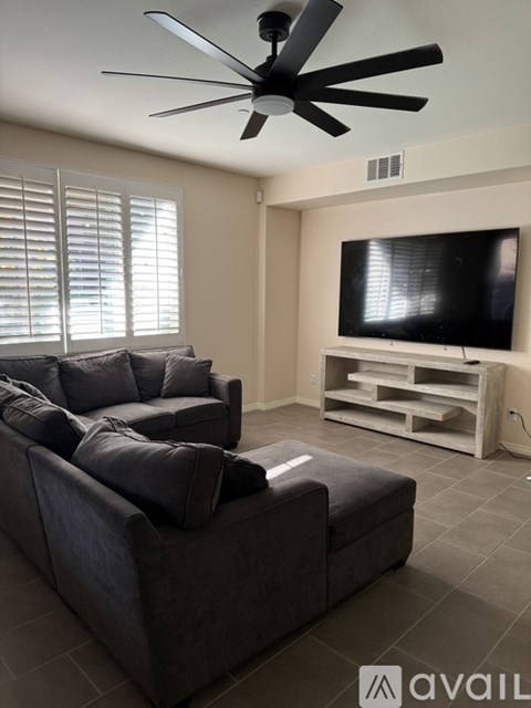 A living room with a grey couch and a black fan.