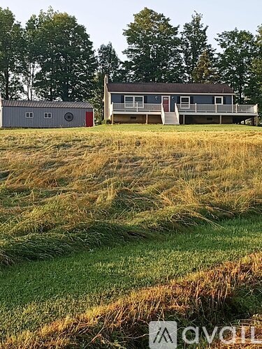 A house with a red door is situated in a field with a shed.