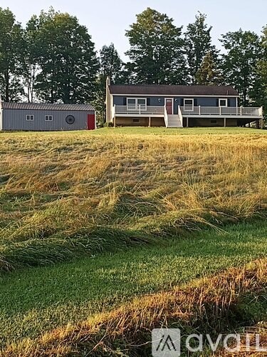 A house with a red door is situated in a field with a shed.