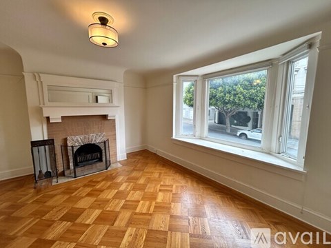 A room with a fireplace and a window overlooking a street.