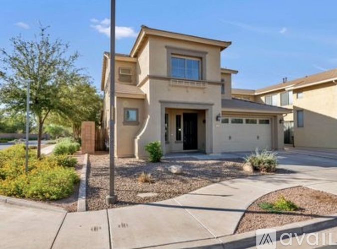 A beige two-story house with a front yard and a tree.