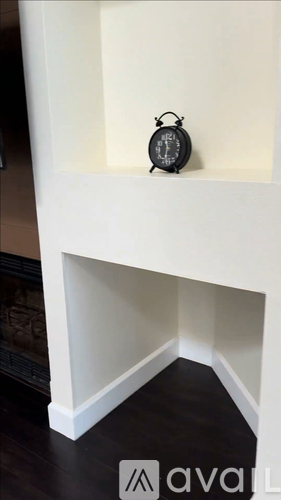 A black clock sits on a white shelf.