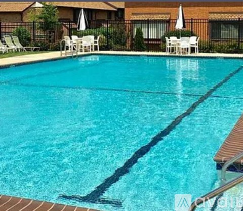 A swimming pool with a brown bench and white chairs.