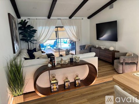 A modern living room with a white sofa, a wooden coffee table with lanterns, and a flat-screen TV mounted on the wall.