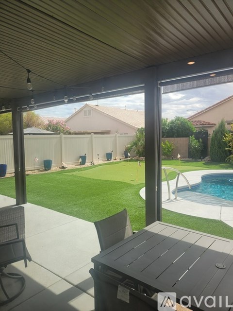 A patio with a table and chairs overlooks a pool and a backyard.