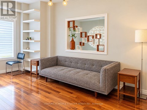 A grey couch sits in a living room with a painting on the wall.