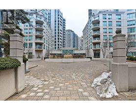 A courtyard with a brick floor and concrete pillars with buildings in the background.