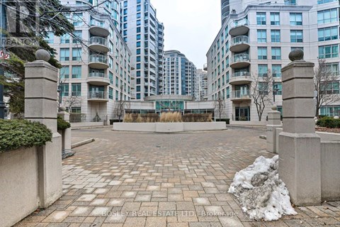 A courtyard with a brick floor and concrete pillars with buildings in the background.