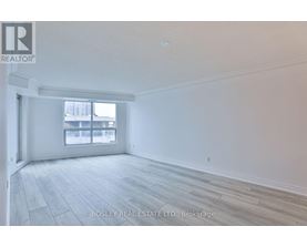 A spacious room with a large window and wooden flooring.