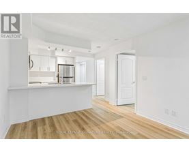 A white room with wooden floors and a kitchen area in the background.