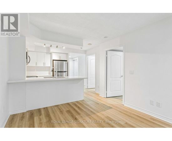 A white room with wooden floors and a kitchen area in the background.