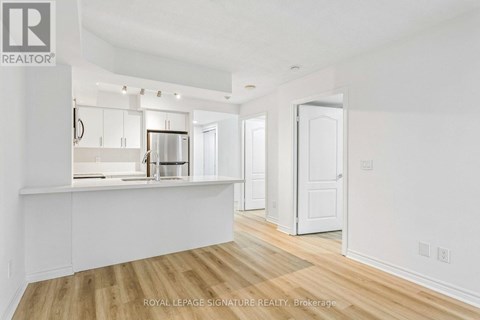 A white room with wooden floors and a kitchen area in the background.