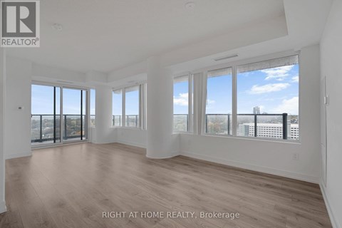A spacious room with wooden flooring and large windows overlooking a cityscape.